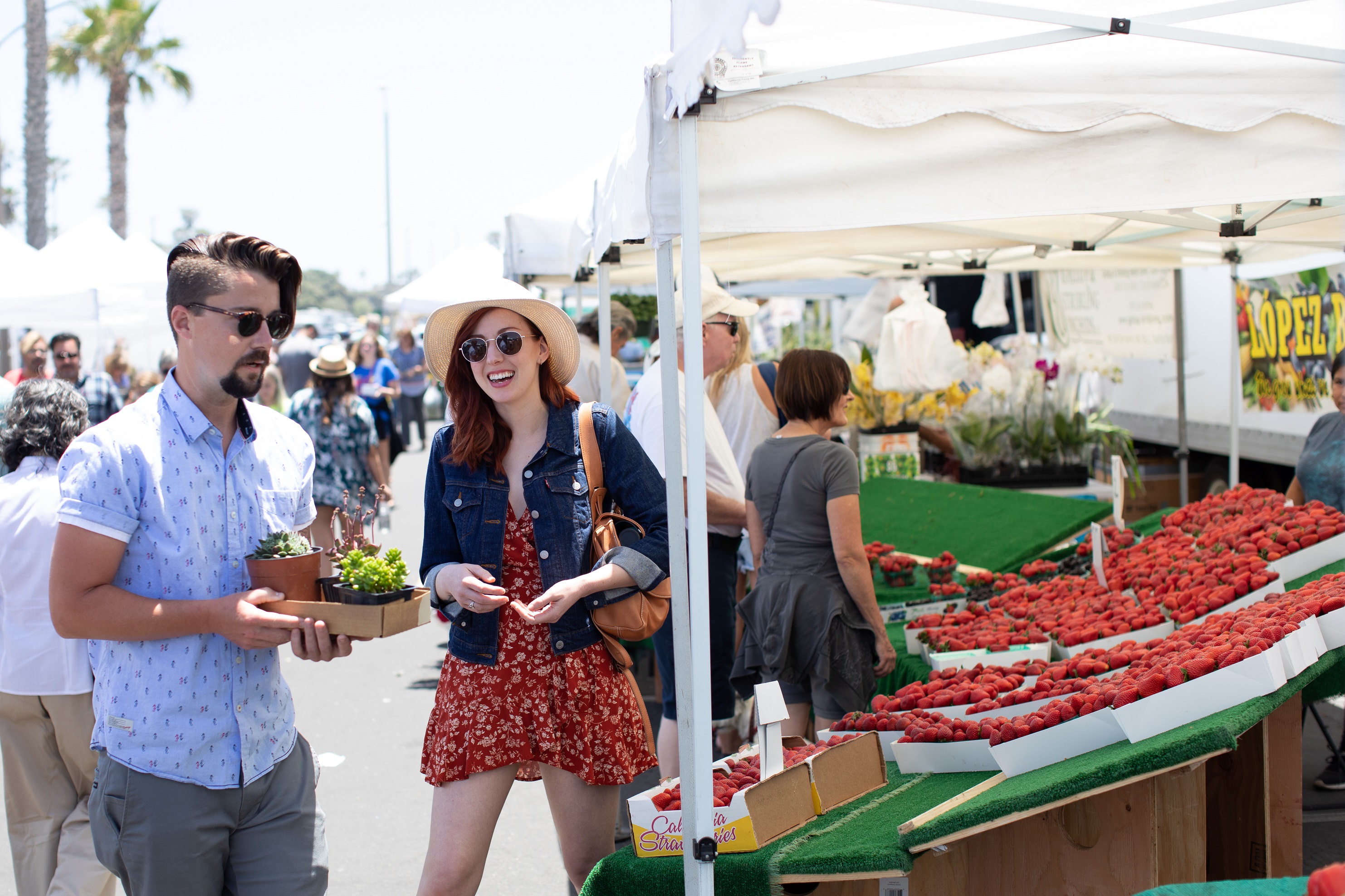 A smiling, stylish couple with new succulents stand next to a table full of strawberry