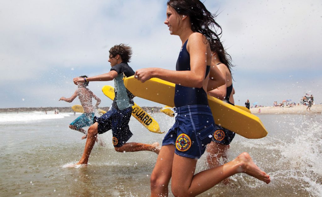 Junior lifeguards carrying rescue buoys race towards the shoreline