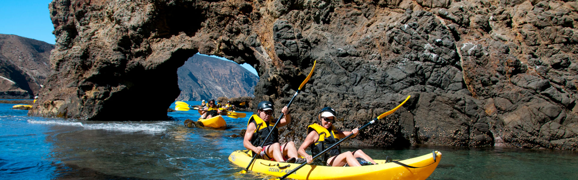 Paddlers move their kayaks through a keyhole rock in the Channel Islands