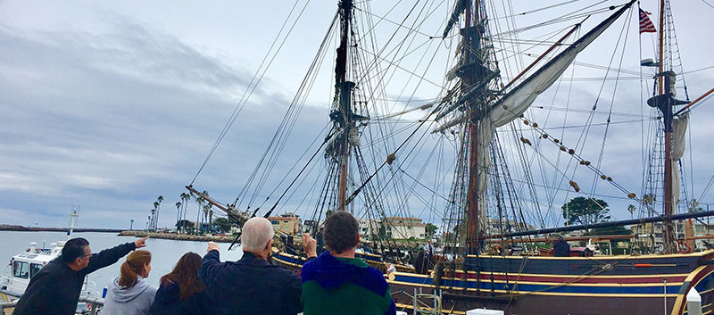 A group looks up at the rigging of a docked tall ship