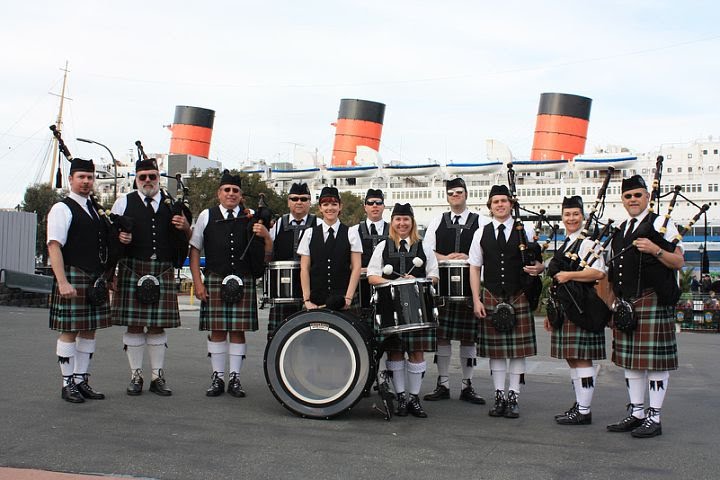 A pipe band in full regalia; wearing kilts and carrying bagpipes and drums, poses for a picture