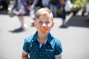 Boy makes faces with half an orange in his mouth