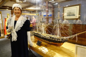 A reenactor at Channel Islands Maritime Museum in front of a large model ship