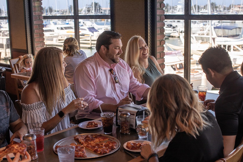 A large group laughs while enjoying pepperoni pizza at Toppers