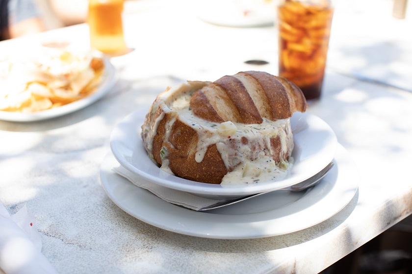 Closeup of a fresh, steaming-hot bread-bowl of clam chowder on a table outdoors