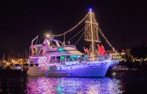 A boat draped in purple and white Christmas lights cruises the harbor at the Oxnard Parade of Lights