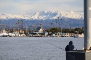 A fisherman is silhouetted against the harbor, snowline low and visible on the mountains in the background