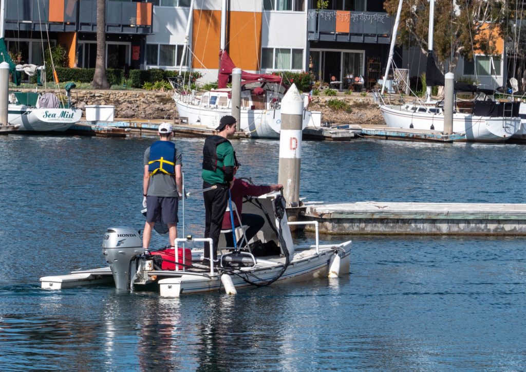 CIH Rowing Club members with nets piloting a flat-deck boat during harbor cleanup